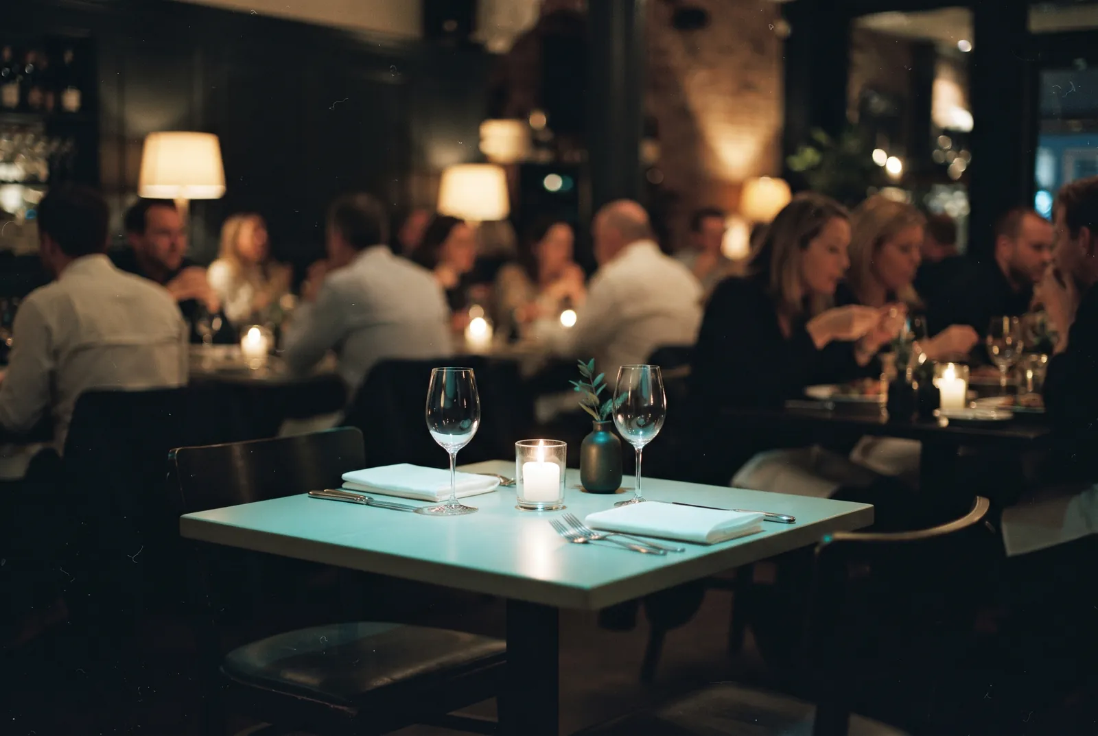 One empty set table in an otherwise busy candlelit restaurant